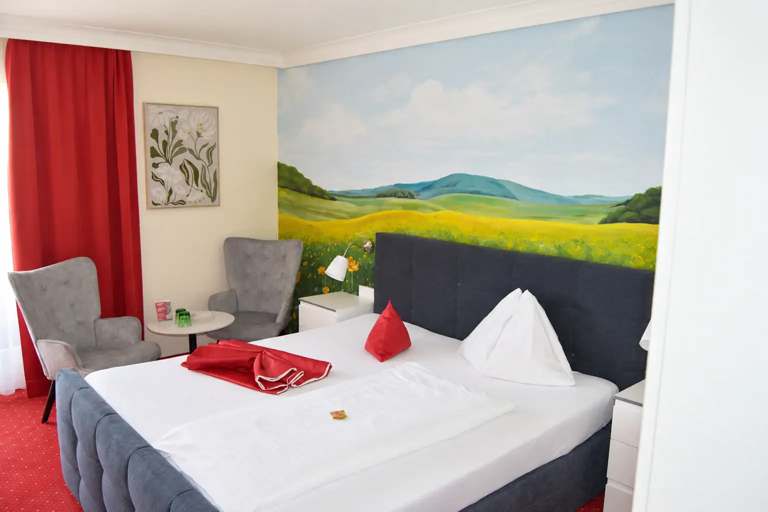 Doppelzimmer mit Landschaftswandbild, gepolstertem Bett und zwei grauen Sesseln